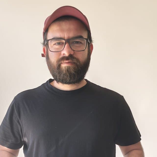 Bilal, in a cap and glasses, against a plain wall.